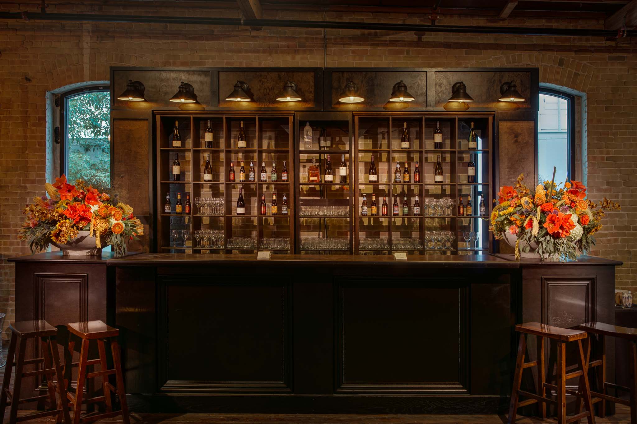 Custom bar installation with warm wood, brass lighting and sculptural florals